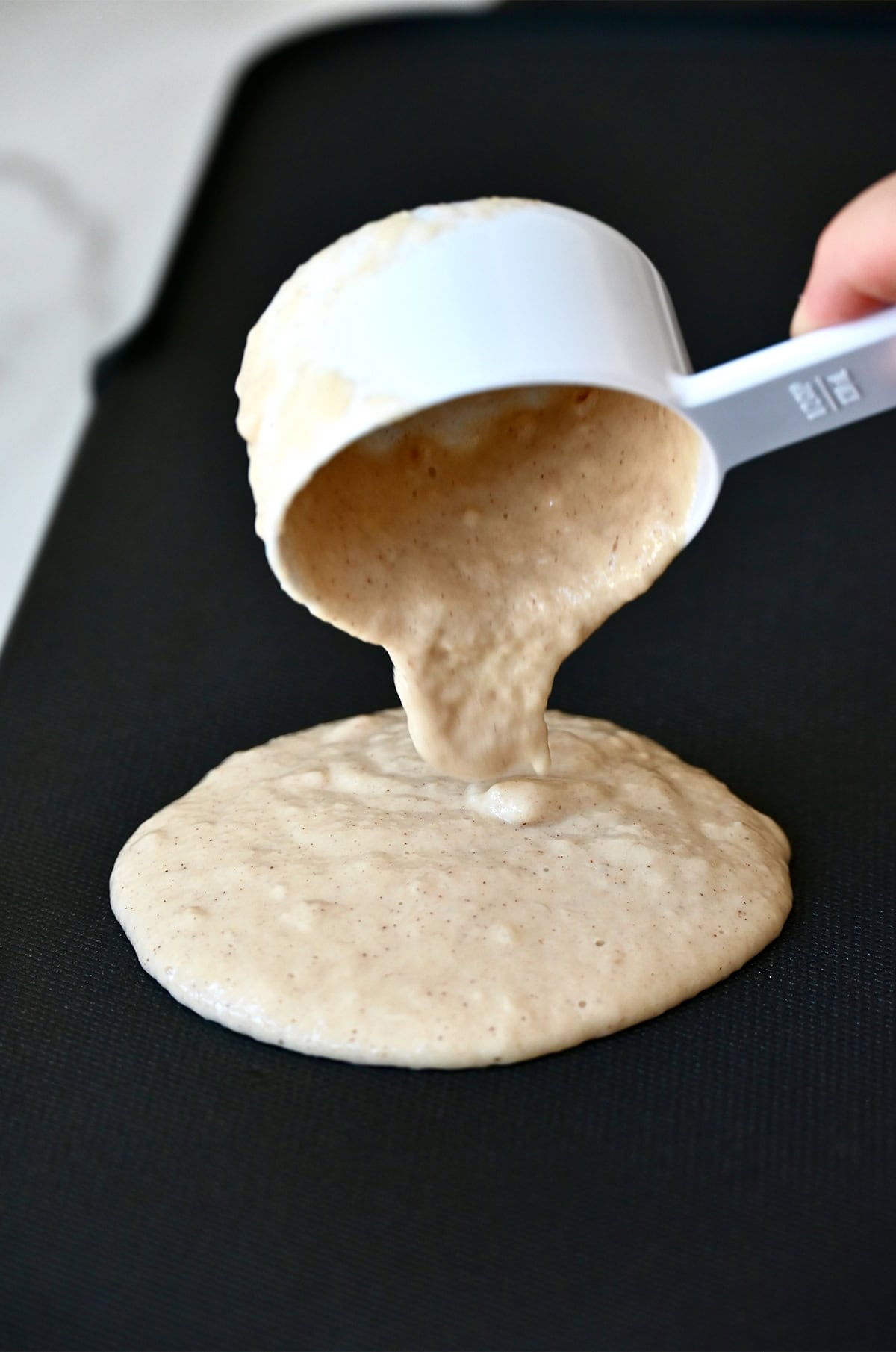 Pouring cinnamon applesauce pancake batter from a measuring cup onto a griddle.