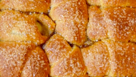 Apple dumplings made with refrigerated crescent rolls in a brown sugar caramel sauce and topped with sanding sugar.
