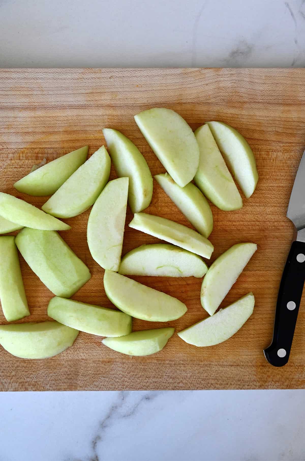 Granny Smith apple slices on a cutting board with a sharp knife.