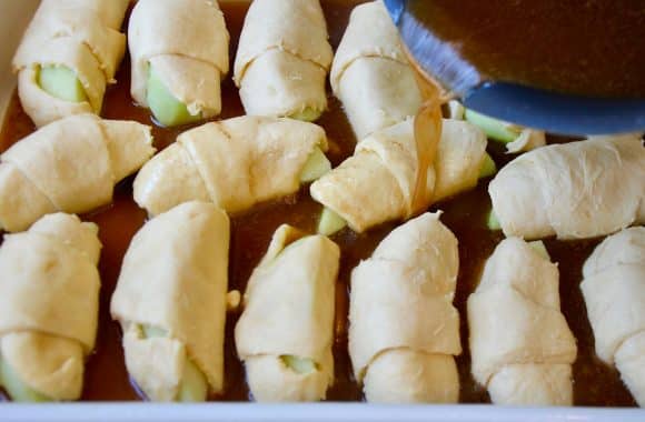 A butter and sugar mixture being poured over a pan of unbaked Crescent Roll Apple Dumplings