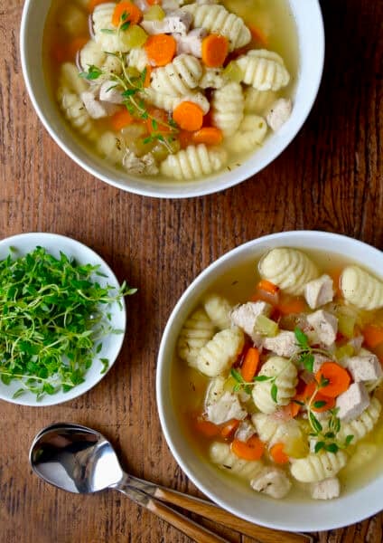 Two bowls of homemade chicken gnocchi soup topped with fresh thyme sprigs.