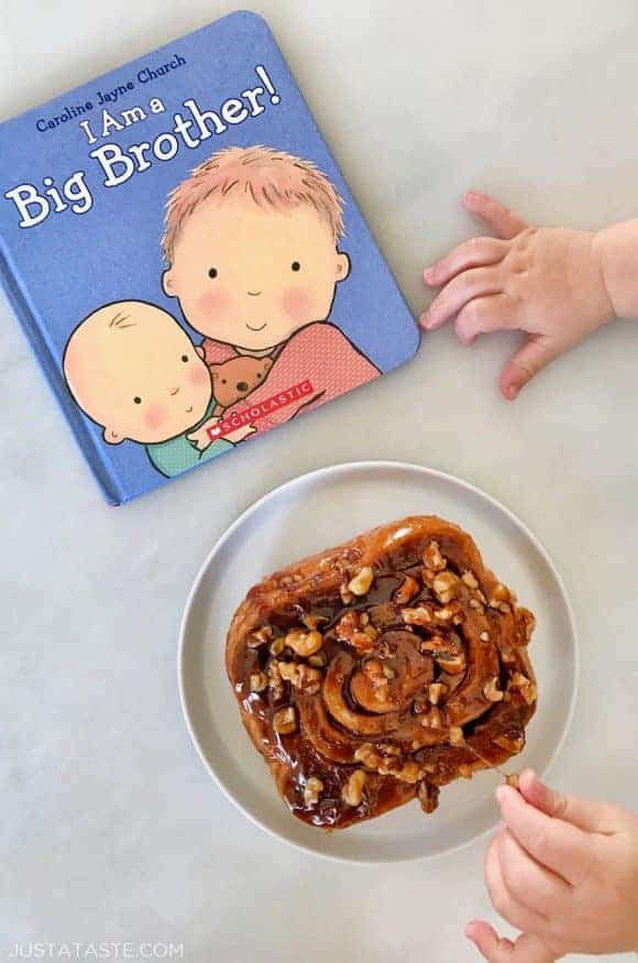 A baby's hands reaching for a sticky bun and a book for a family of four announcement