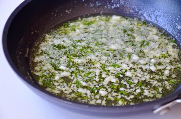 A sauté pan filled with melted garlic butt and herbs 