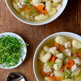 Gnocchi chicken soup in two bowls with a bowl of fresh thyme