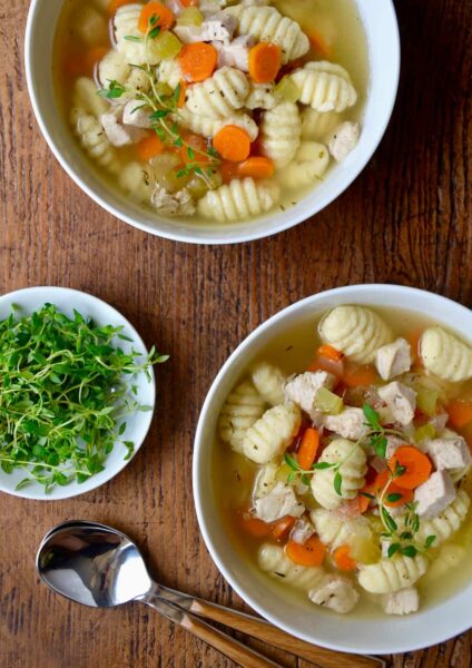 Gnocchi chicken soup in two bowls with a bowl of fresh thyme