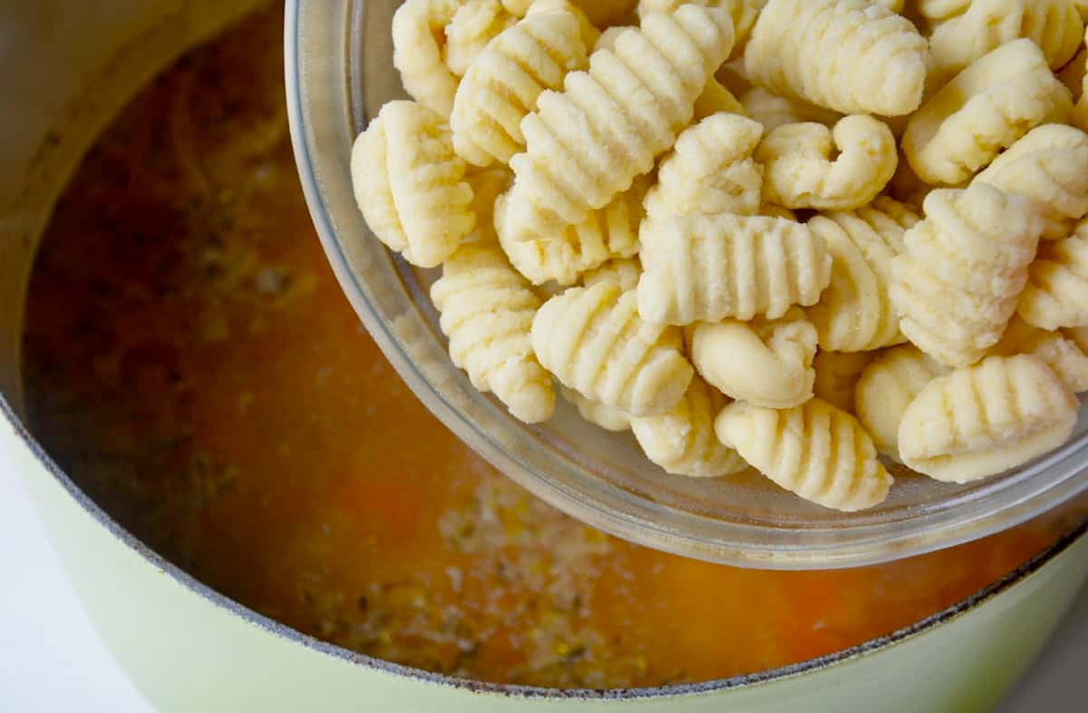 Adding store-bought gnocchi to a stockpot with broth and sauteed aromatics to make a homemade soup.