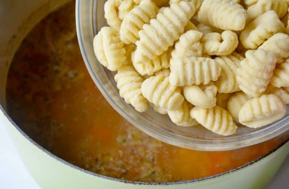 Fresh gnocchi being added to a stock pot of chicken soup