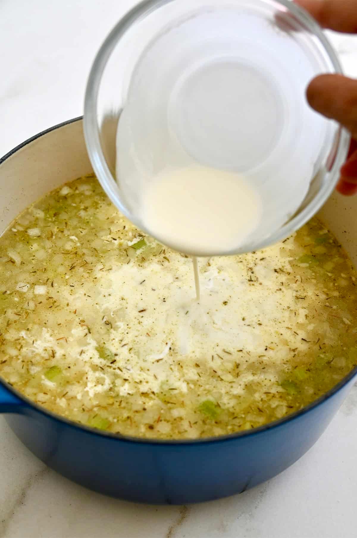 Heavy cream being poured into a pot of chicken gnocchi soup for an optional creamy variation.
