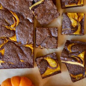 Pumpkin cheesecake brownies on tan parchment paper cut into squares with sugar pumpkins