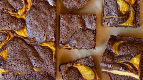 Pumpkin cheesecake brownies on tan parchment paper cut into squares with sugar pumpkins