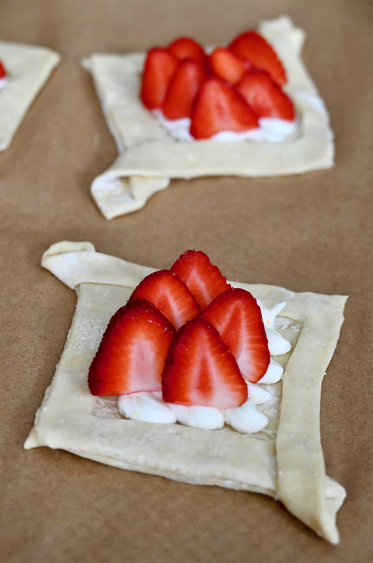 Unbaked cheese Danish topped with fresh strawberries on parchment paper.