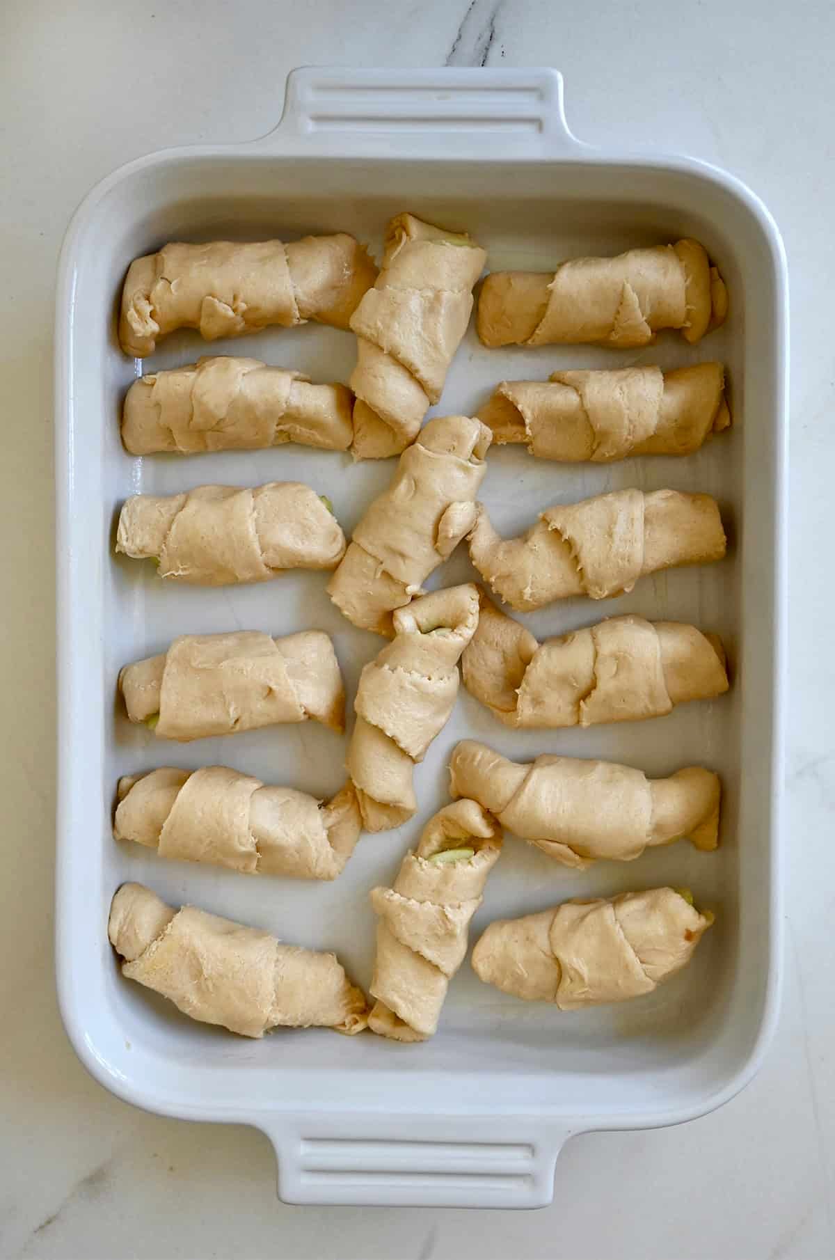 Unbaked crescent roll apple dumplings arranged in a 13x9-inch baking dish before adding sauce.