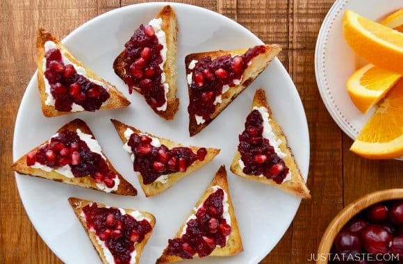 A white plate with triangular cheese toasts topped with orange cranberry relish