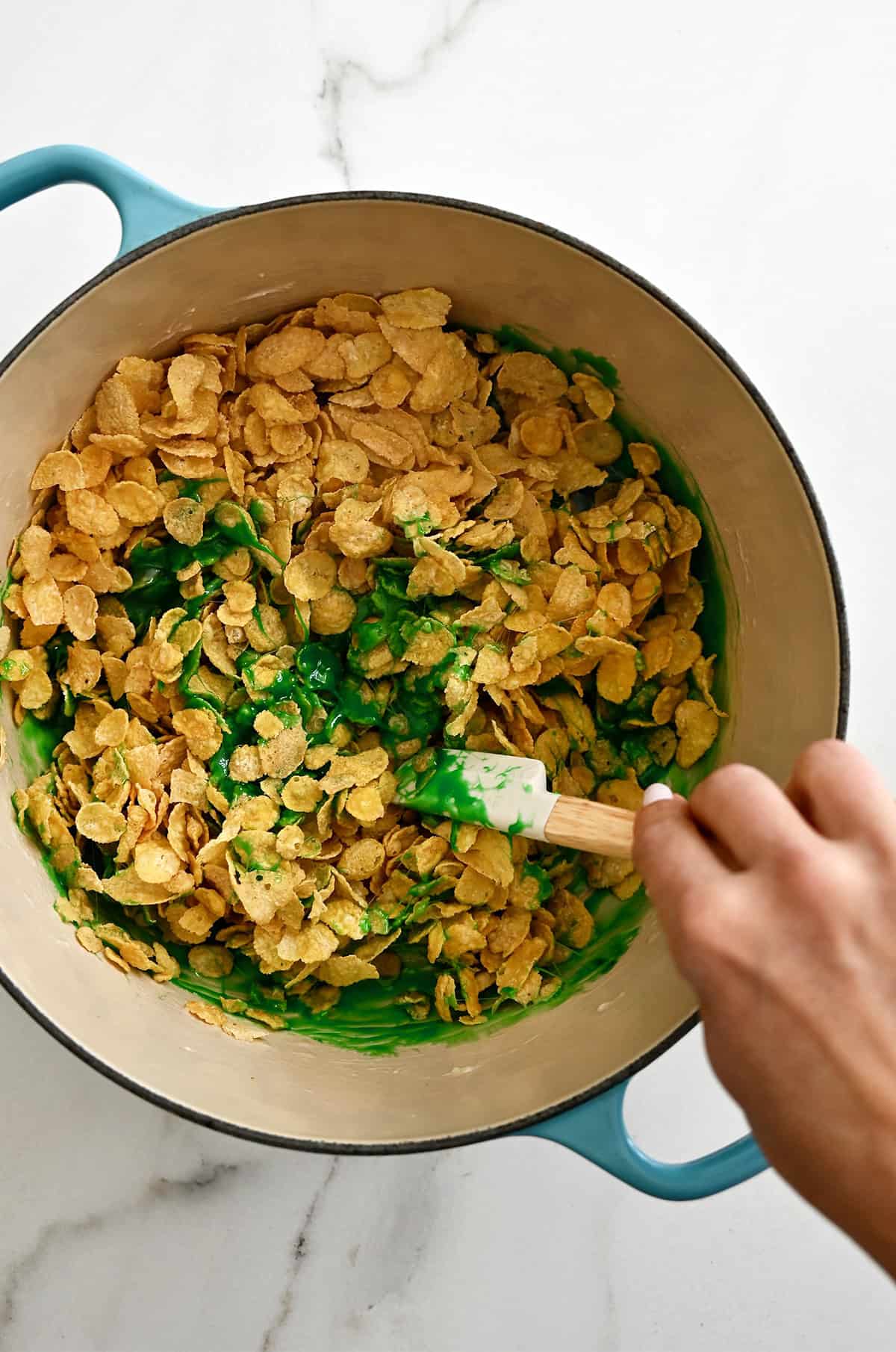 Cornflakes being coated in a green marshmallow-butter mixture to make wreath cookies.