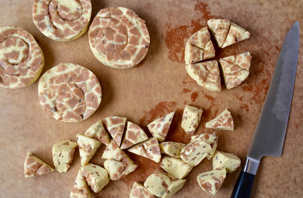 Canned cinnamon rolls are spread out on a cutting board and being cut into chunks for cinnamon roll casserole.