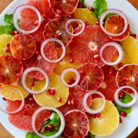 A white plate containing sliced citrus fruits and red onions