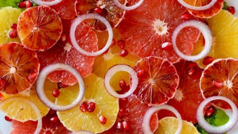 A white plate containing sliced citrus fruits and red onions