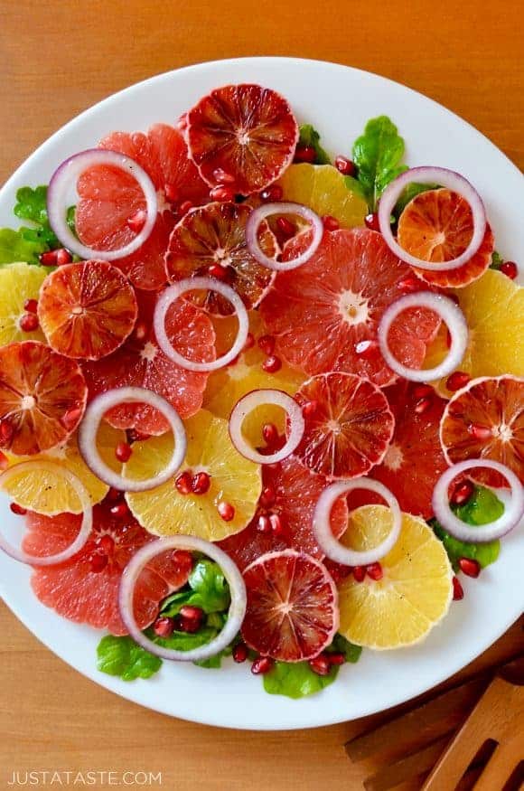 A white plate containing sliced citrus fruits and red onions