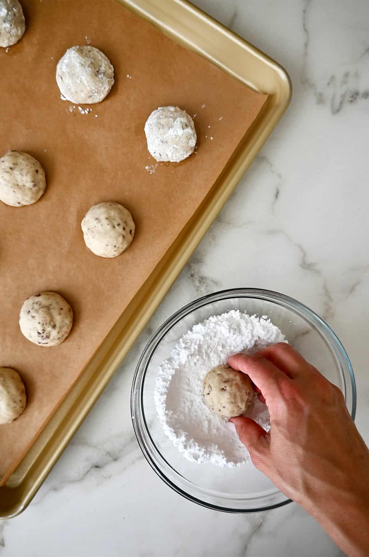 Coating baked snowball cookies in powdered sugar.