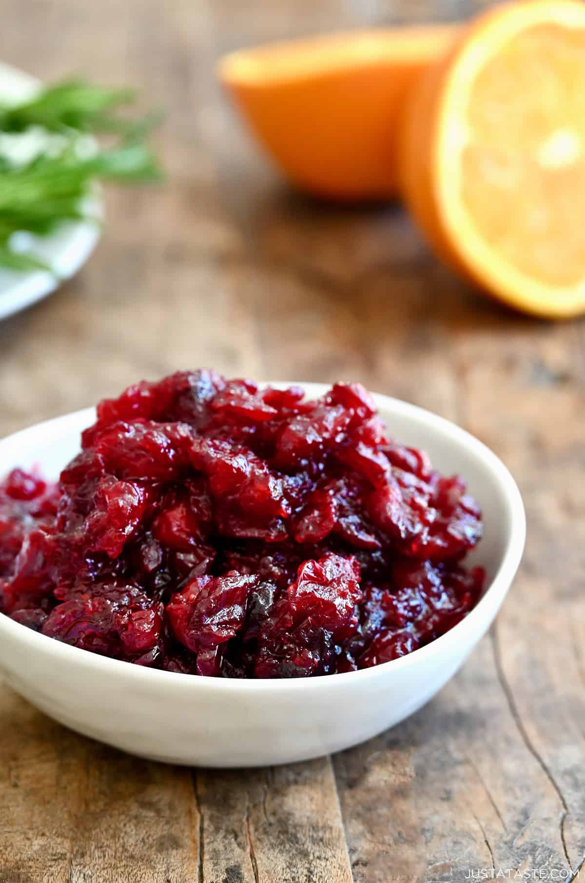 Homemade cranberry sauce in a white bowl with an orange cut in half nearby.