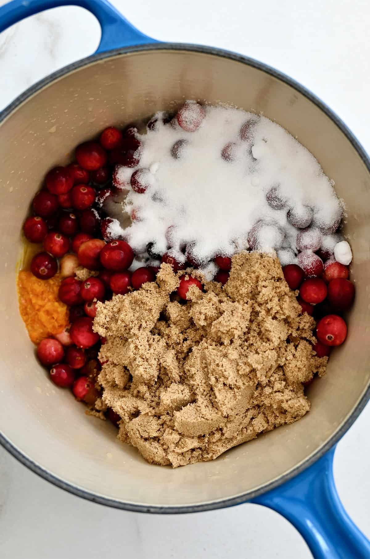 Cranberries, orange juice and zest, white sugar, and brown sugar in a saucepan before being reduced into cranberry sauce.