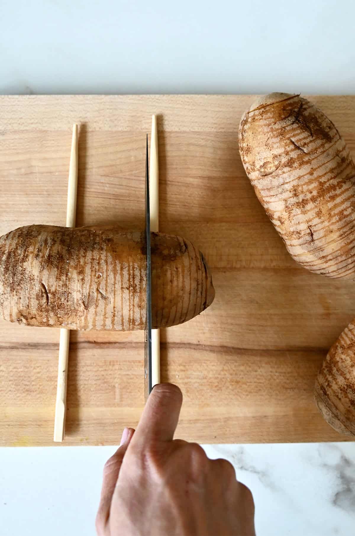 Slicing a russet potato between chopsticks to make hasselback potatoes without cutting all the way through.