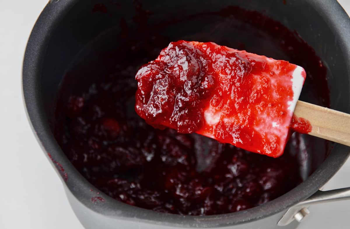 A spatula covered in homemade cranberry sauce above a saucepan containing more sauce.