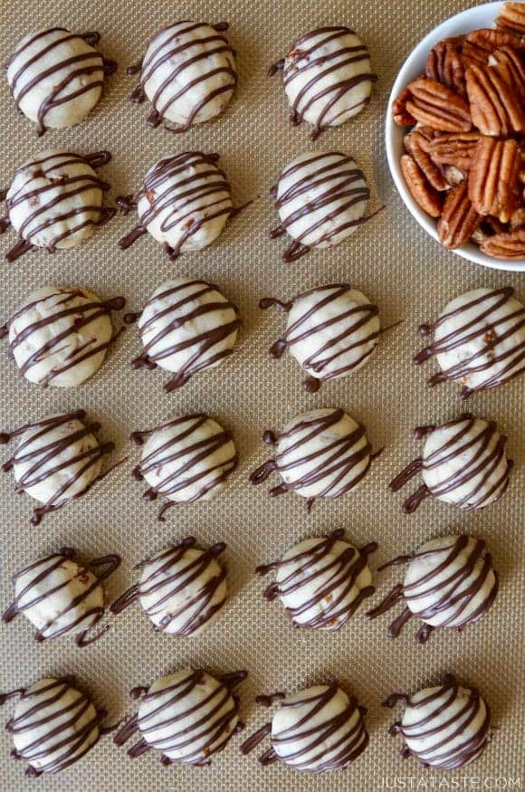 A baking sheet with rows of Easy Pecan Balls and a bowl of pecans