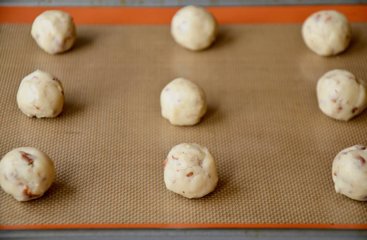 Rolled balls of pecan cookie dough are spaced out on a Silpat-lined baking sheet.