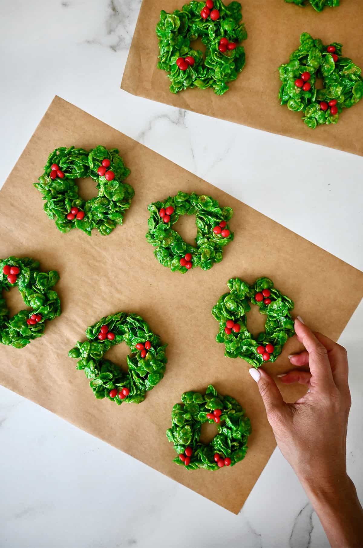 Christmas wreath cookies are cooling on a sheet of wax paper.