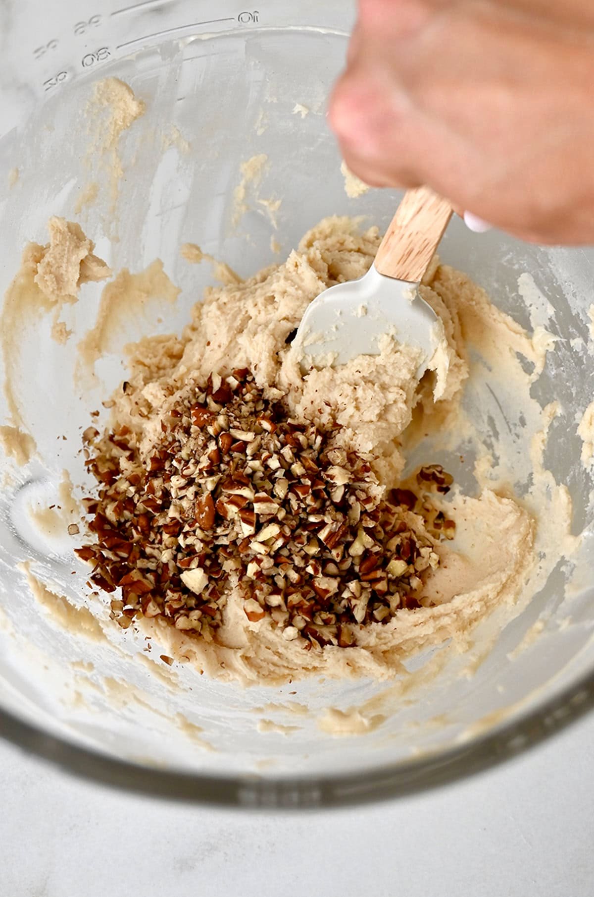 Finely chopped pecans being folded into snowball cookie dough.