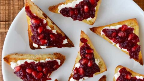 A white plate containing triangular toasts with orange cranberry relish
