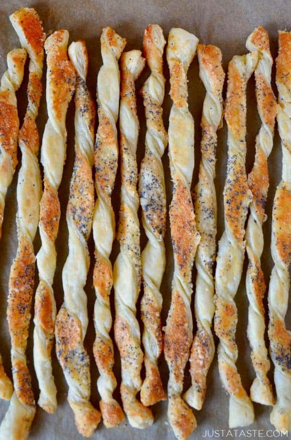 A close up of cheesy puff pastry twists on a baking sheet lined with parchment paper