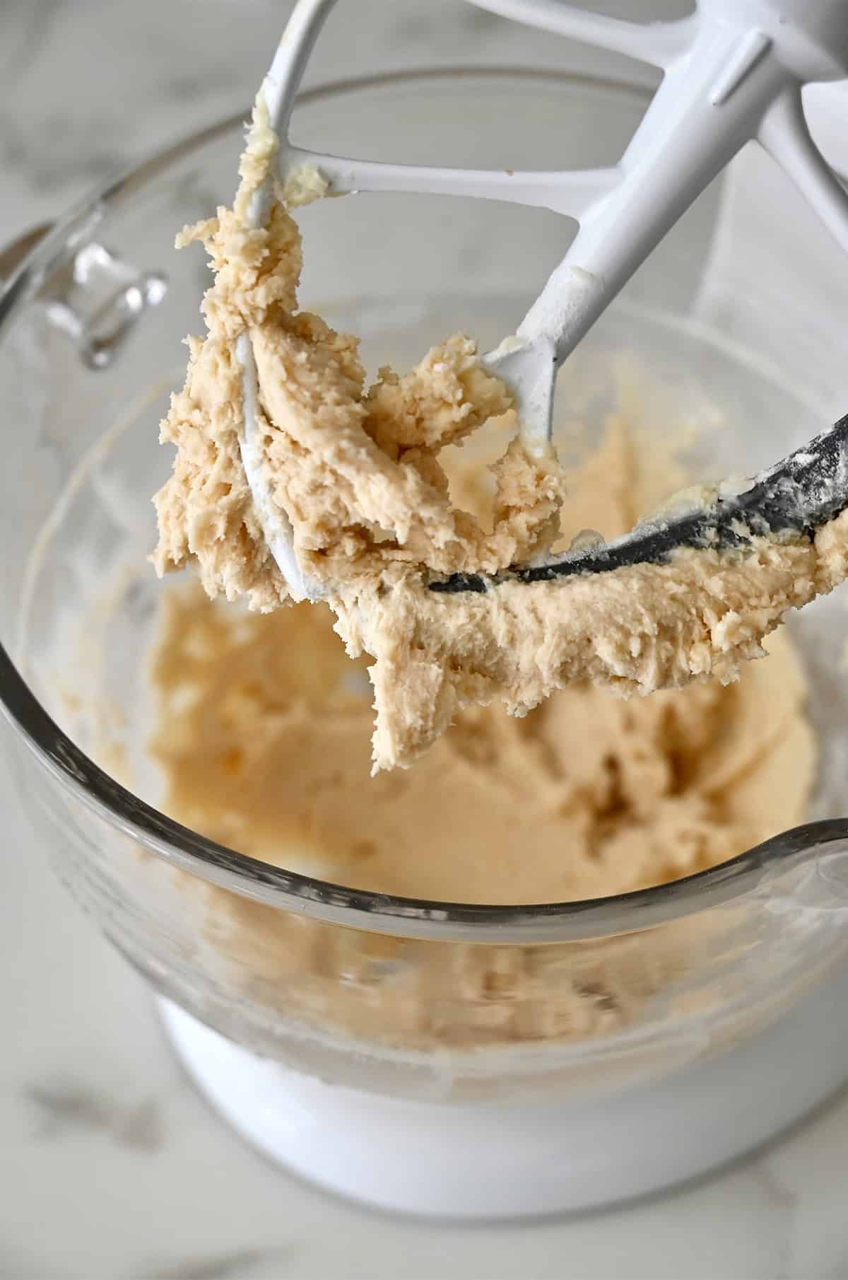 Snowball cookie dough covering the paddle attachment of a stand mixer.