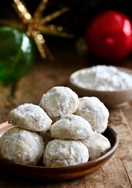Snowball cookies on a plate with holiday ornaments nearby.