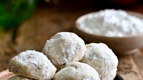 Snowball cookies on a plate with holiday ornaments nearby.