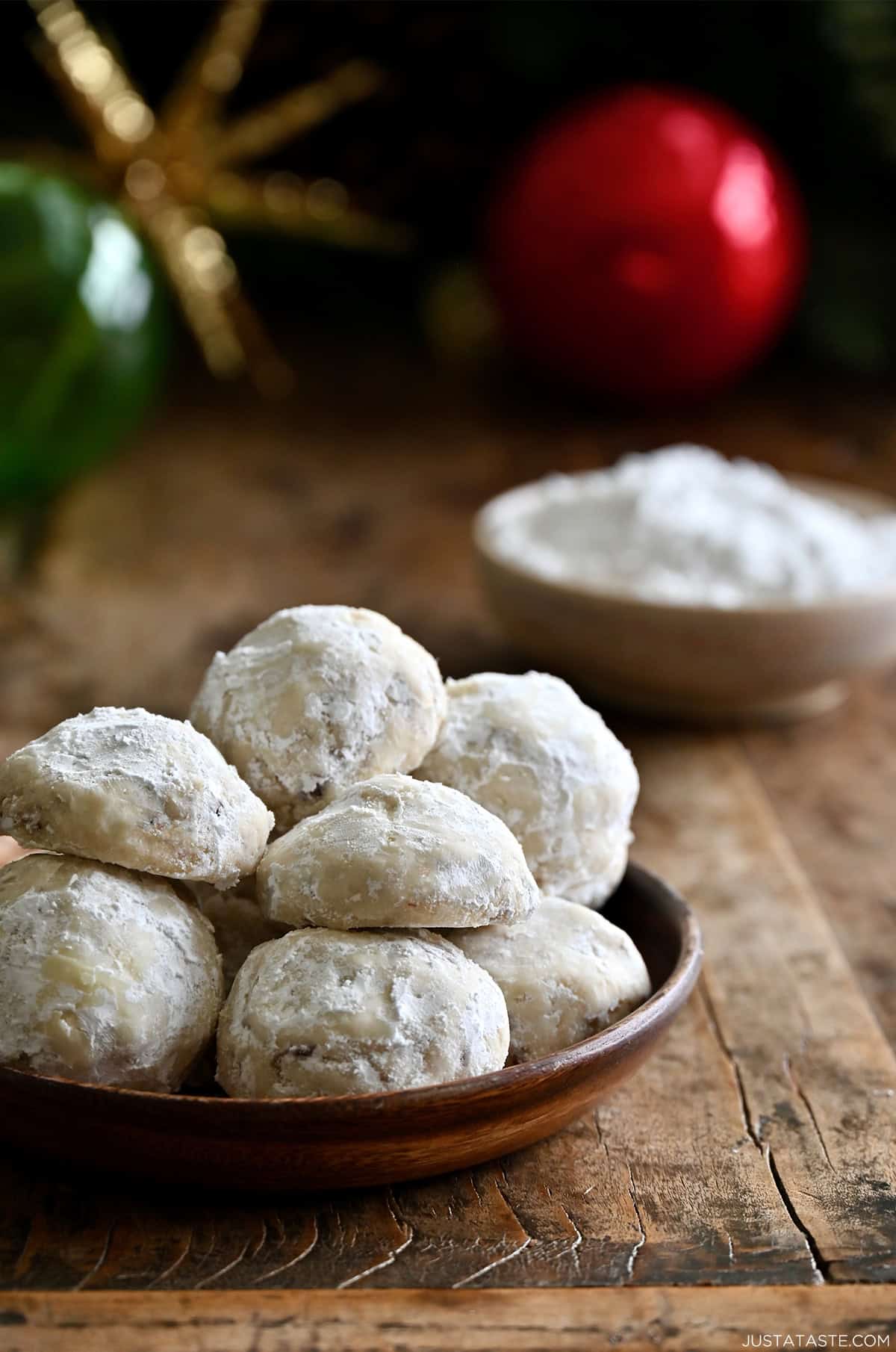 Snowball cookies on a plate with a bowl of powdered sugar in the background.