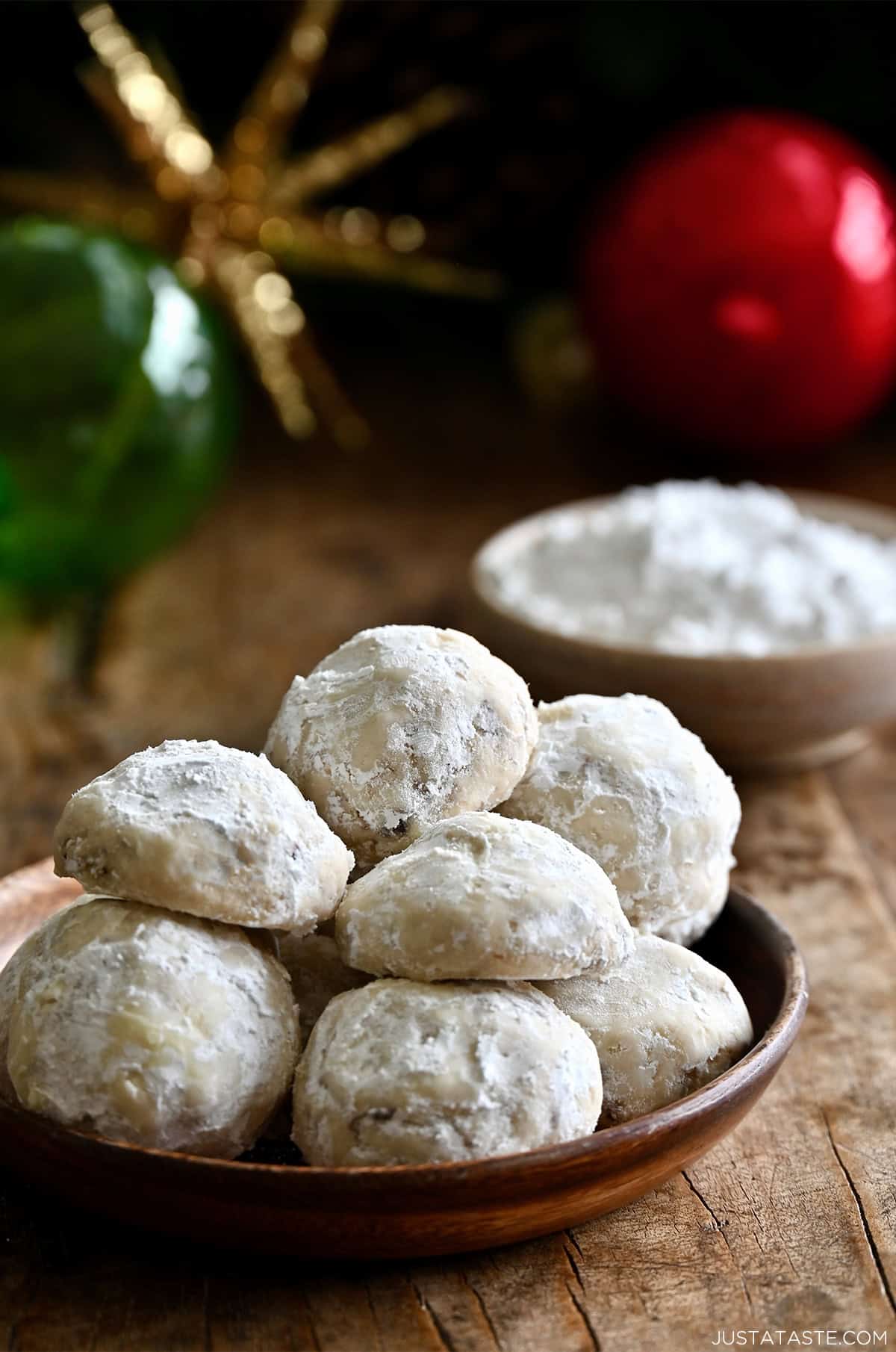 Snowball cookies on a plate with holiday ornaments nearby.