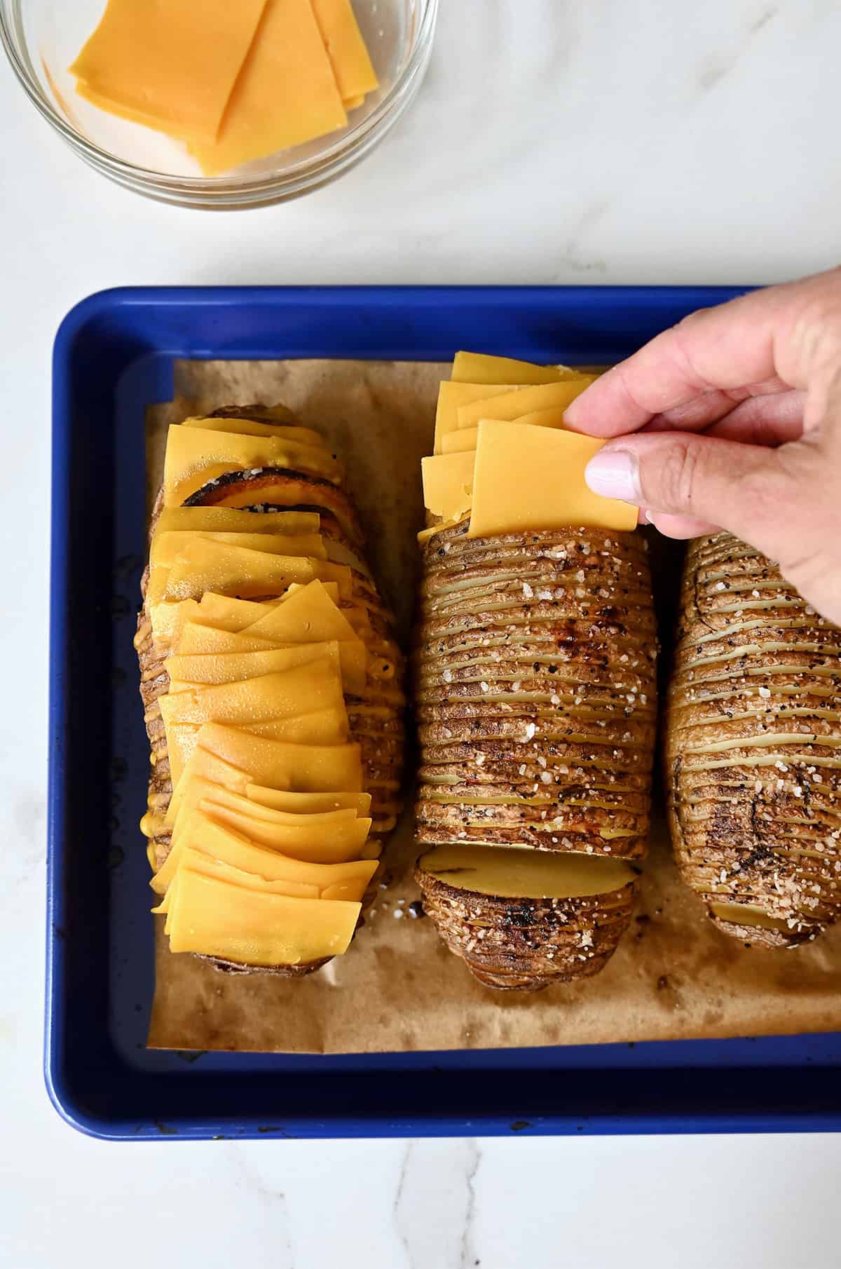 Stuffing slices of cheddar cheese into a baked hasselback potato.