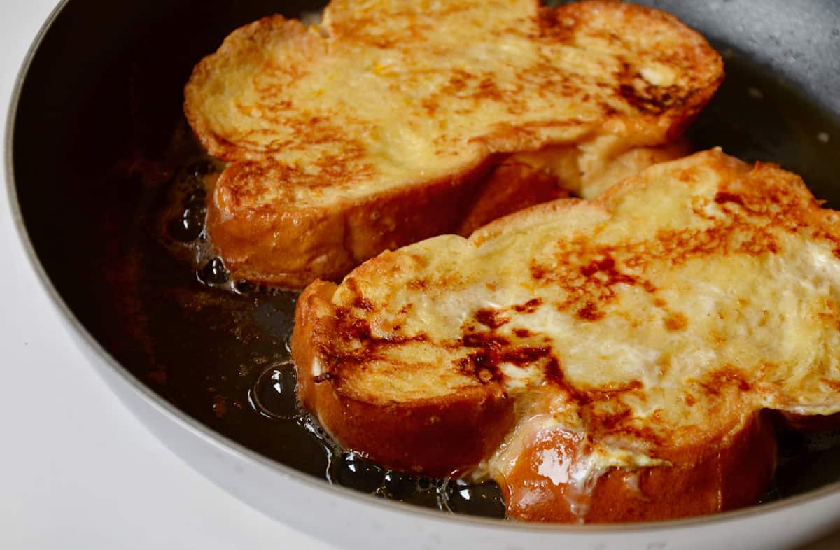 Two pieces of challah French toast sizzle in a saute pan.