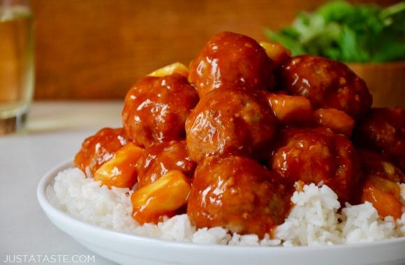A white plate containing white rice and Sweet and Sour Meatballs with pineapple