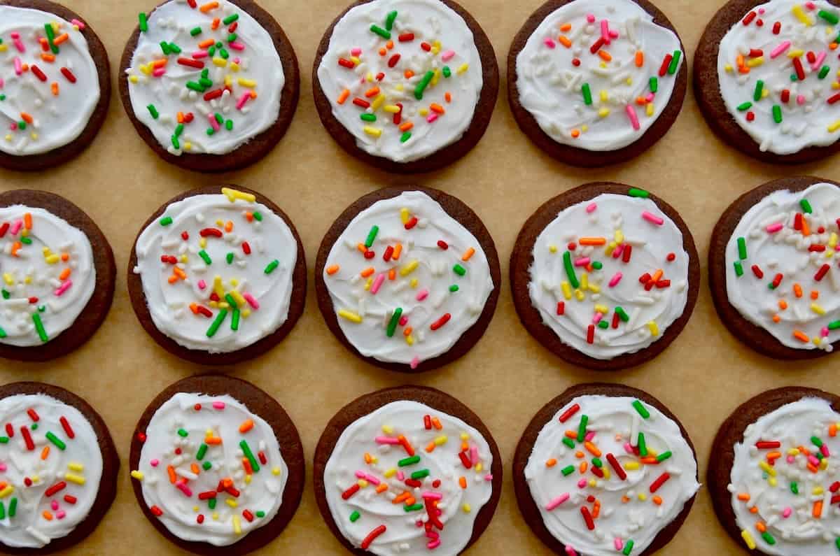 Chocolate sugar cookies topped with buttercream frosting and rainbow sprinkles.