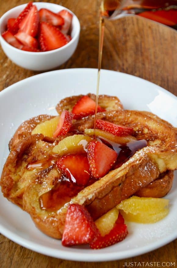 A white plate containing Challah French Toast with syrup being drizzled on top