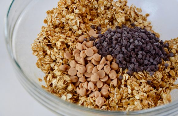 A glass bowl containing oat mixture with peanut butter chips and mini chocolate chips