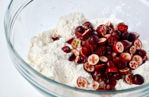 A glass bowl containing flour, sugar and cranberries