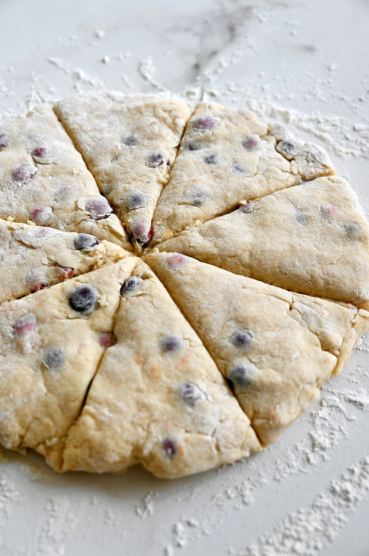 A circle of orange cranberry scone dough cut into eight wedges.