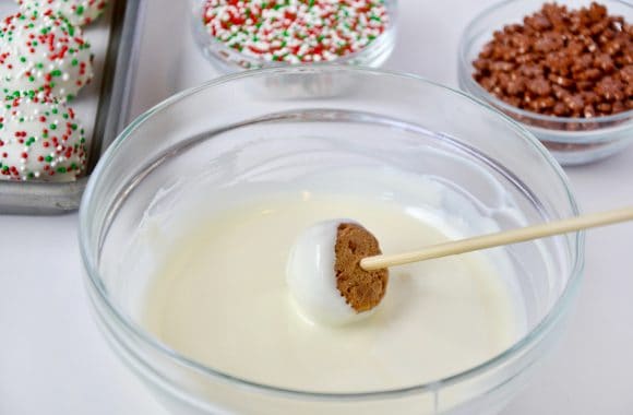 A gingerbread cookie ball being dipped in melted white chocolate