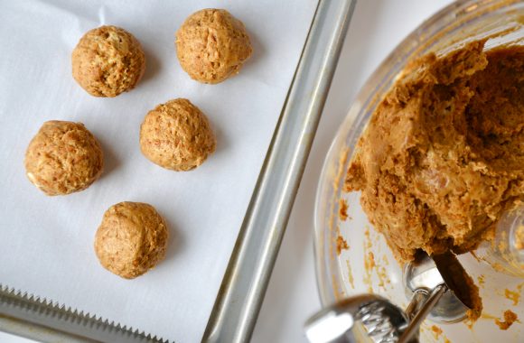 A baking sheet with gingerbread cookie balls and a food processor bowl with ice cream scoop
