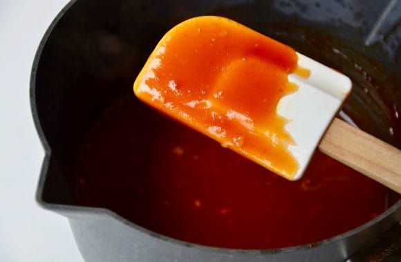 White spatula with homemade sweet and sour sauce with more in saucepan in background