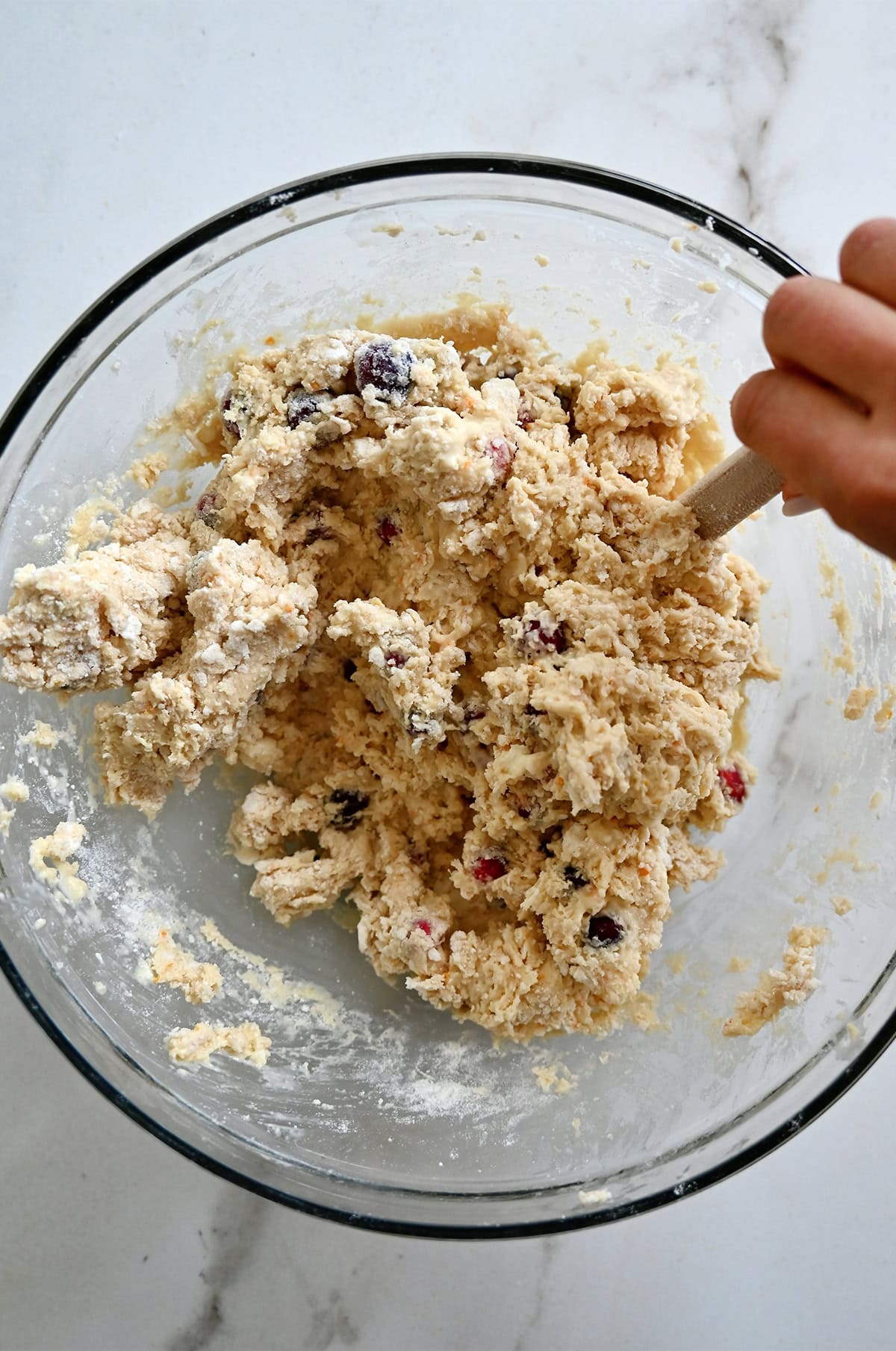 Using a spatula to gently fold all the ingredients together to make orange cranberry scones.